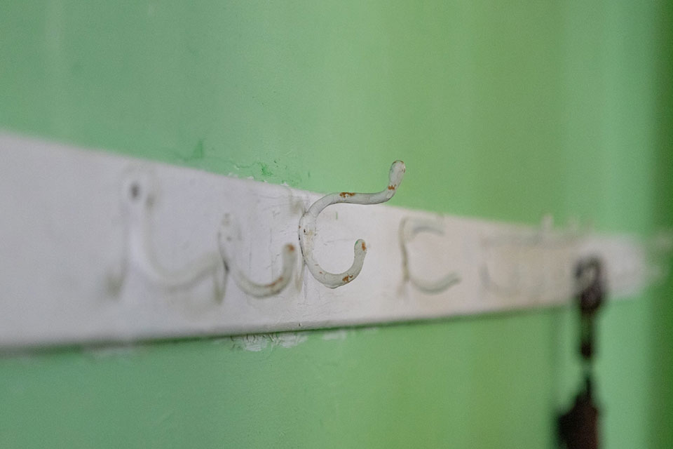 A photograph of a worn rack of coat hooks mounted on a white board, which is itself mounted on a lime-green wall