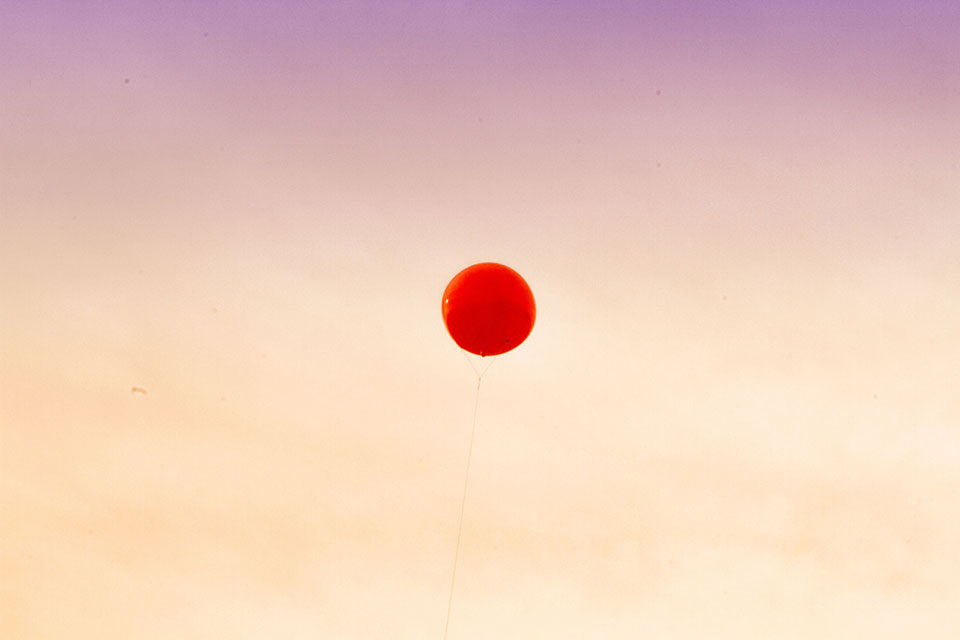 A red balloon hovers mid-frame against a dusking sky