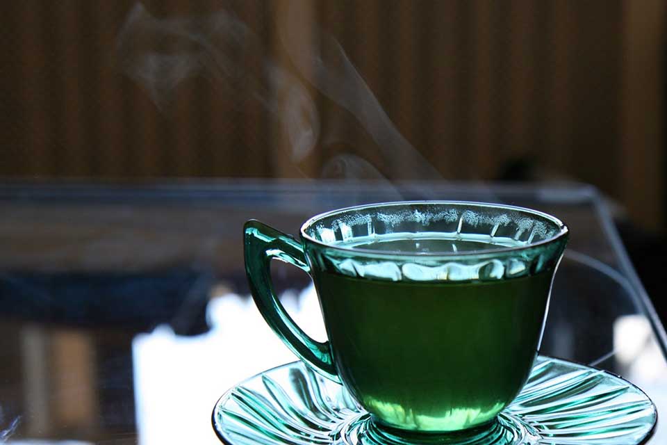 A photograph of a cup of tea. The cup is clear and the tea is green