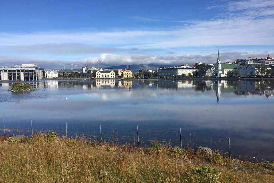 The city of Reykjavik framed in the foreground by a lake and in the background by cloud-capped mountains