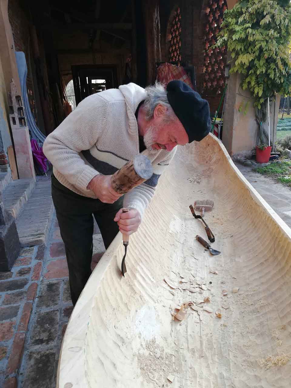 A photograph of a man chiseling out a canoe