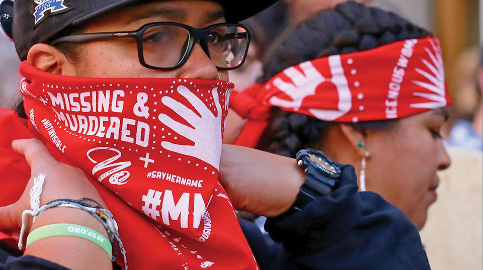 A close photograph of a protestor, whose red bandana reads Missing and Murdered