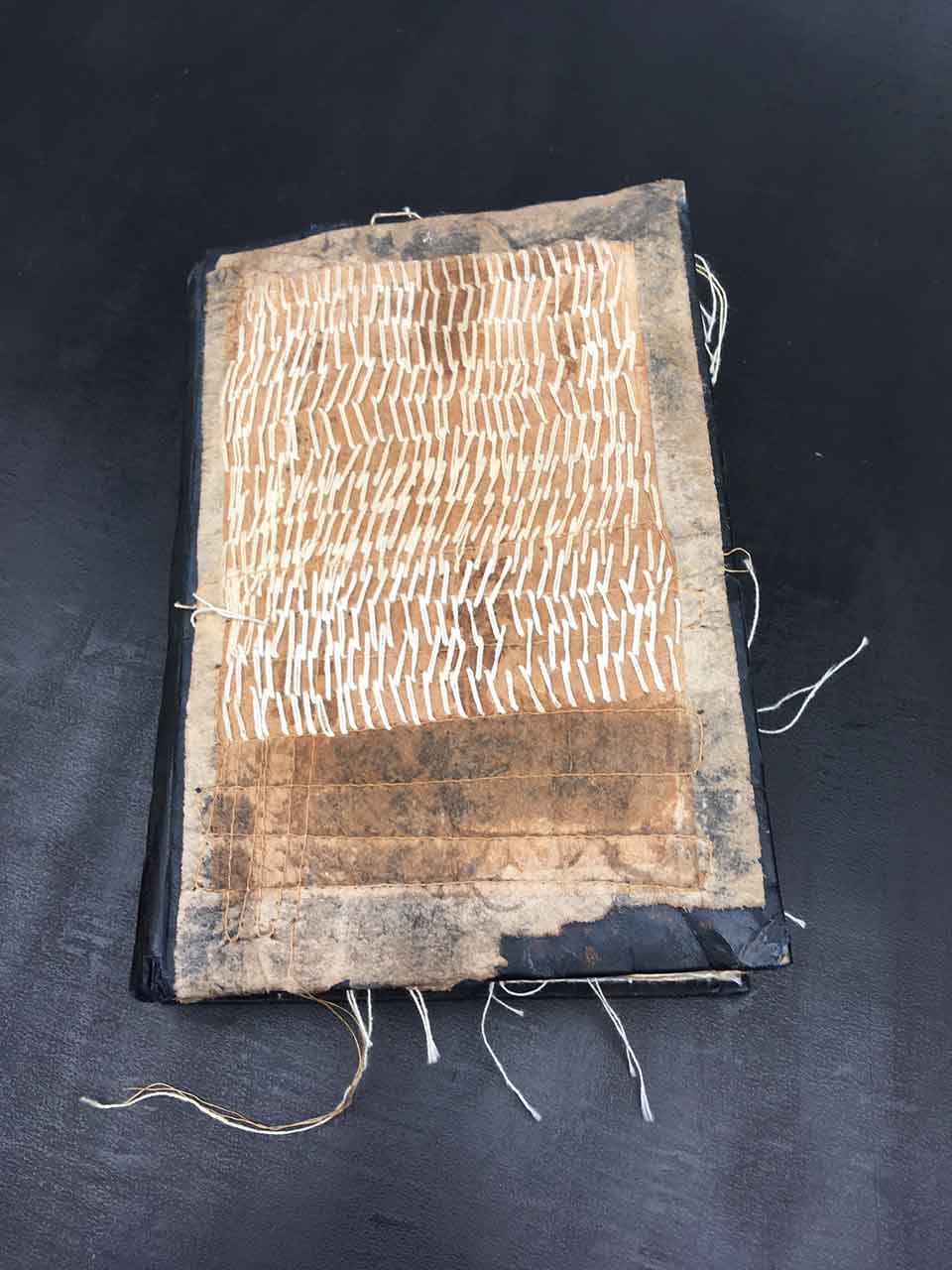 A photograph of a roughly hewn book with thick thread stitched into the cover