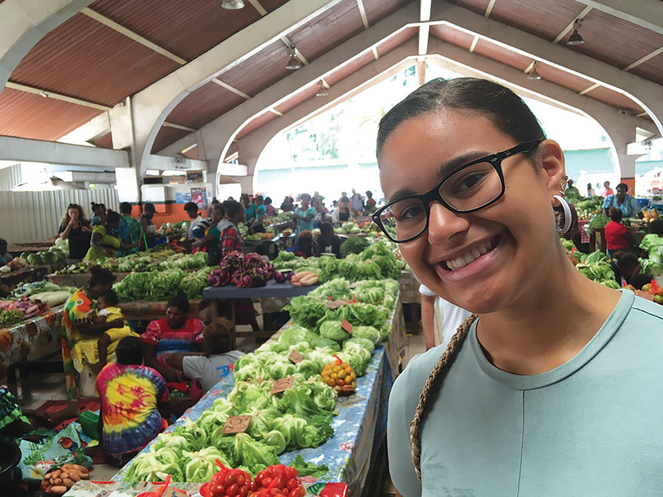 A photograph of a woman smiling at the camera with an open air market in the background