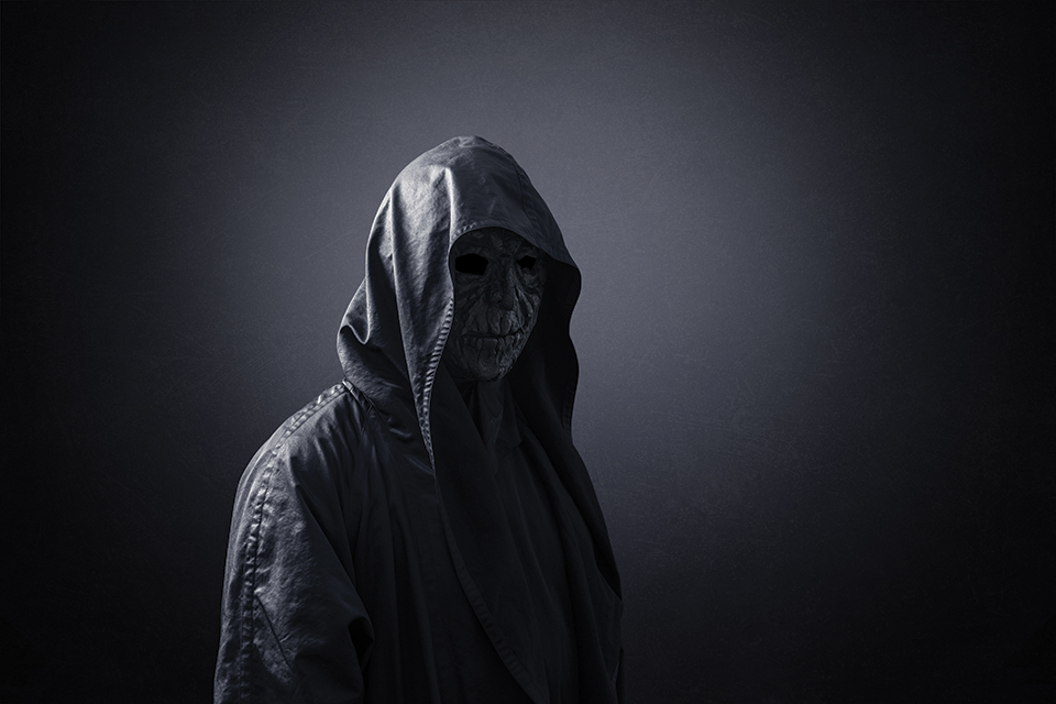 A dimly-lit figure, hooded and shrouded in black