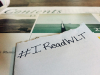 The hashtag #IReadWLT written on a sheet of paper with the magazine in the background