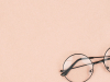 A photograph of round lensed glasses resting against a peach background