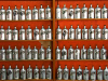 A photograph of long rows of hair tonic in metallic bottles against a red-orange wall