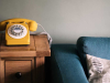 A photograph of a yellow telephone sitting on a wood table next to a blue couch