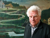 Author Tankred Dorst standing in front of a painting of a road winding up a mountain