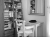 A black and white photo of a chair and desk sitting next to a bookshelf