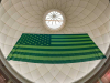 A photograph of an American flag, reimagined in green, hanging from a domed ceiling, as seen from below