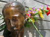 A photograph of a the head of a bronze statue of a female figure. Flowers have been placed behind the statue's head
