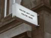 A sign mounted on the corner of a building. The sign reads, ”You are not lost. You are here.”