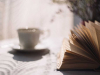 A teacup sits, out of focus, next to a book on a table.
