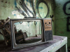 A photograph of a broken television with no screen in a room tagged with graffiti on the walls