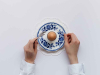 A photo looking down on a single egg on a fine piece of blue china, framed by two hands preparing to eat the egg