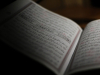 An open book written in Arabic, mostly shrouded in shadow