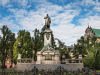 A monument to poet Adam Mickiewicz, surrounded by trees under a blue sky dotted with clouds