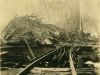A sepia-toned photograph of a set of railroad tracks, which have been destroyed, with a city in rubble in the background