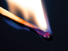 A close-up photograph of a wood match burning