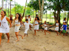 Children, dressed in white, dance in a line while holding hands