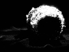 A black and white photo of a ball of aluminum foil, shrouded in darkness, except for a strip of focused light on its right side. 