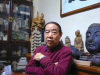 Author Jing Pingwa sits, arms crossed casually, in front of a number of religious icons