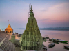 A tall stone temple dominates the shoreline of a wide river, bathed in the colors of sunset