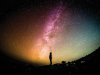A photograph of a silhouette of a person who is gazing up at the night sky, which is blazoned with color