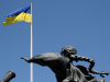 A metal sculpture of a woman looking up at the flag of Ukraine