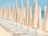 A row of umbrellas over reclining benches stretching into the distance by edge of the ocean against a light blue sky