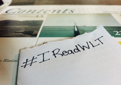 The hashtag #IReadWLT written on a sheet of paper with the magazine in the background