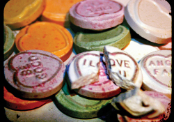 A pile of conversation hearts with one that reads "I Love You" broken at the top of the pile