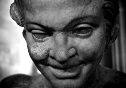 A black and white photograph of a grimacing face rendered in stone