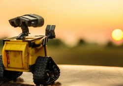 A photograph of a toy robot with a setting sun in the background