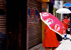 A woman, dressed in red, walks down the street, her face obscured by a red umbrella