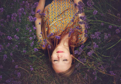 A photograph looking down on a young woman who is laying in the grass, eyes closed. Photo by Amy Treasure on Unsplash.
