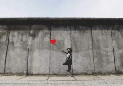 A painting of a girl in black and white holding a red balloon on a drab gray wall