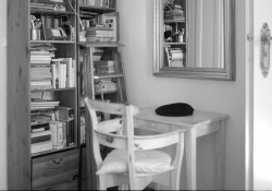 A black and white photo of a chair and desk sitting next to a bookshelf
