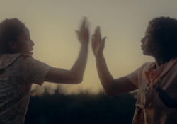 Two women standing face to face at sunset, arms raised in front of them until their hands almost touch