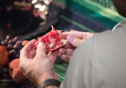 A photograph taken over a man's shoulder as he opens a pomegranate.
