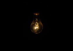 A photograph of a very dim lightbulb that is all but being swallowed by the darkness surrounding