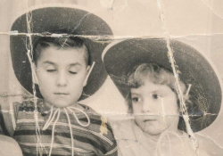An old black and white photograph of a young boy and girl, both wearing cowboy hats, sitting next to one another