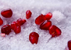 A photograph of dark crimson pomegranate seeds delicately laid out on snow