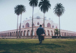 A man in the foreground walks toward Humayun's Tomb, partially shrouded in fog, in New Delhi