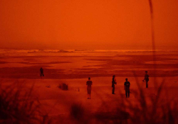 A photograph of figures on a beach. The photograph is heavily colored in red and orange tones.