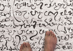 A pair of bared feet rest on a cloth covered in a non-English script.