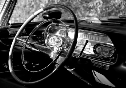 A black and white photograph of the interior of a vintage Cadillac with the focus on the steering column and gauges