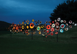 Many round objects, painted like bird's eye are mounted to poles and illuminated at night